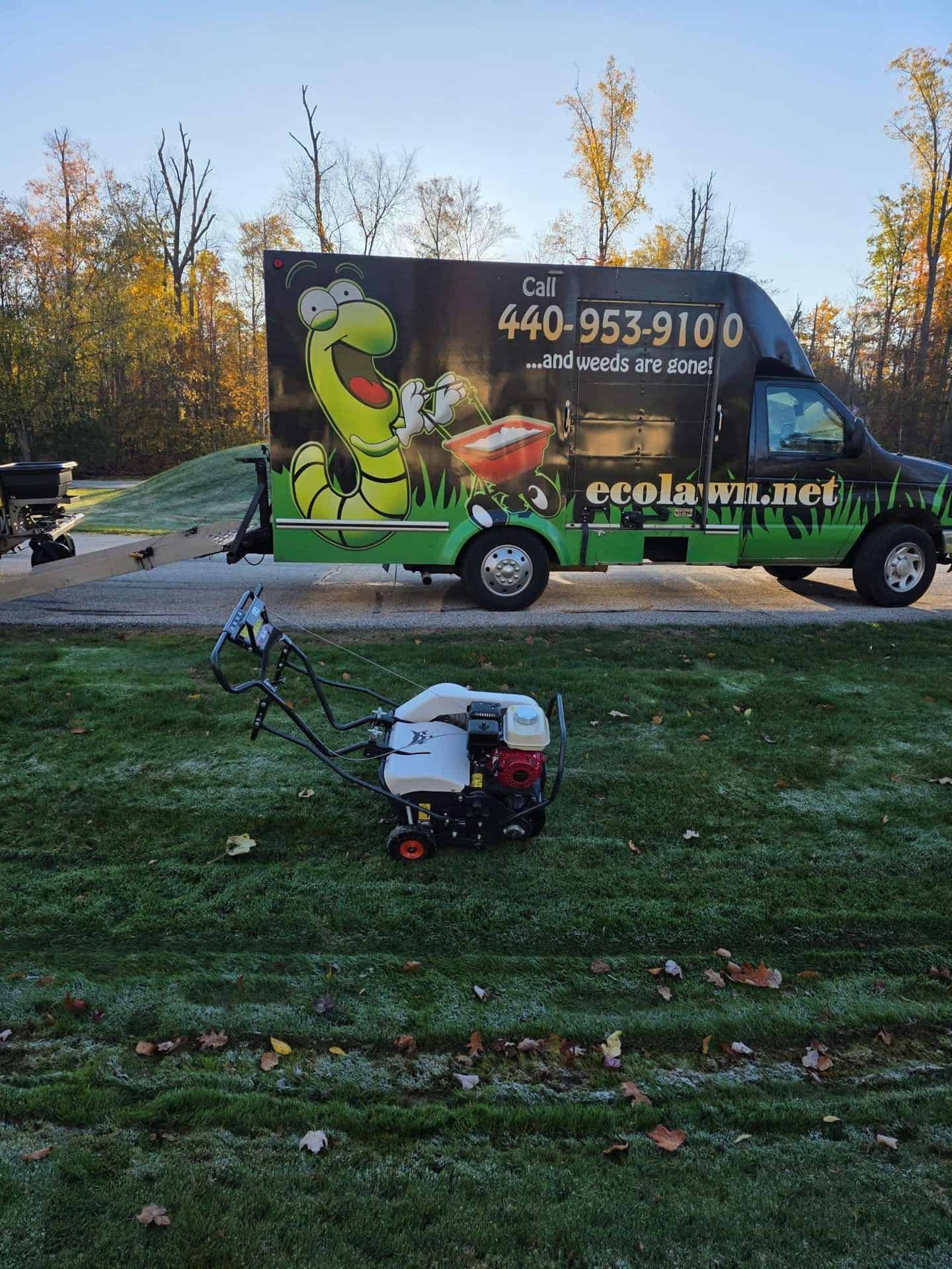 A core aerator parked on a frosty morning lawn in front of an Ecolawn service truck